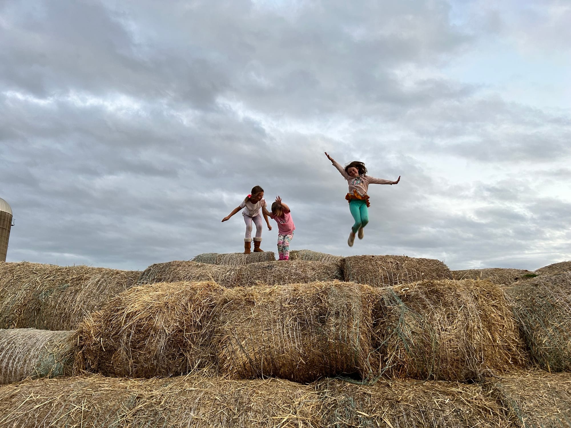Three kids jumping on hay bales at sunset